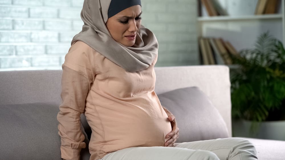 Pregnant woman in hijab feeling belly pain, risk of misbirth, prenatal care Hijabi woman about to give birth in labor