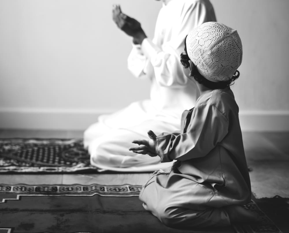 Muslim boy learning how to make Dua to Allah father son on prayer mat